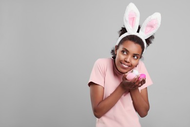 Photo of Happy African American woman in bunny ears headband with Easter egg on gray background. Space for text