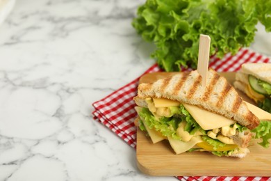 Photo of Wooden board with tasty sandwich on white marble table, space for text