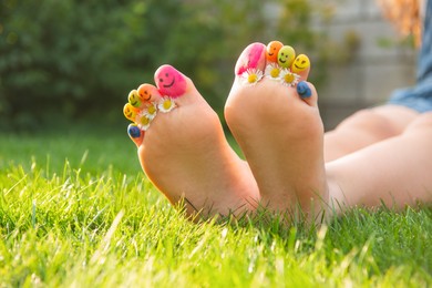 Photo of Teenage girl with drawn smiling faces and chamomiles between toes outdoors, closeup