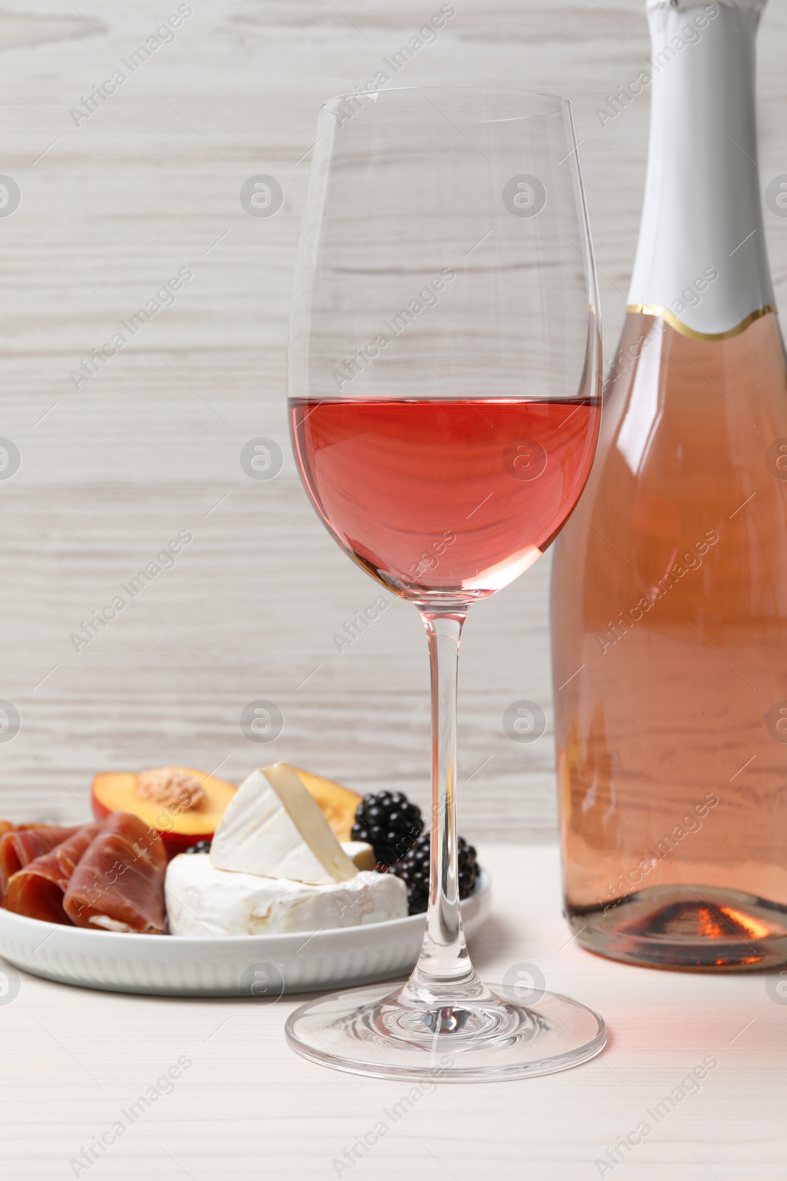 Photo of Delicious rose wine and snacks on white wooden table