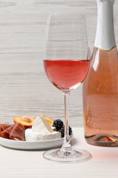Photo of Delicious rose wine and snacks on white wooden table