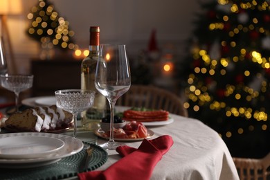 Photo of Christmas table setting with bottle of wine, appetizers and dishware in room