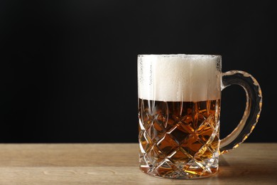Photo of Mug with fresh beer on wooden table against black background. Space for text