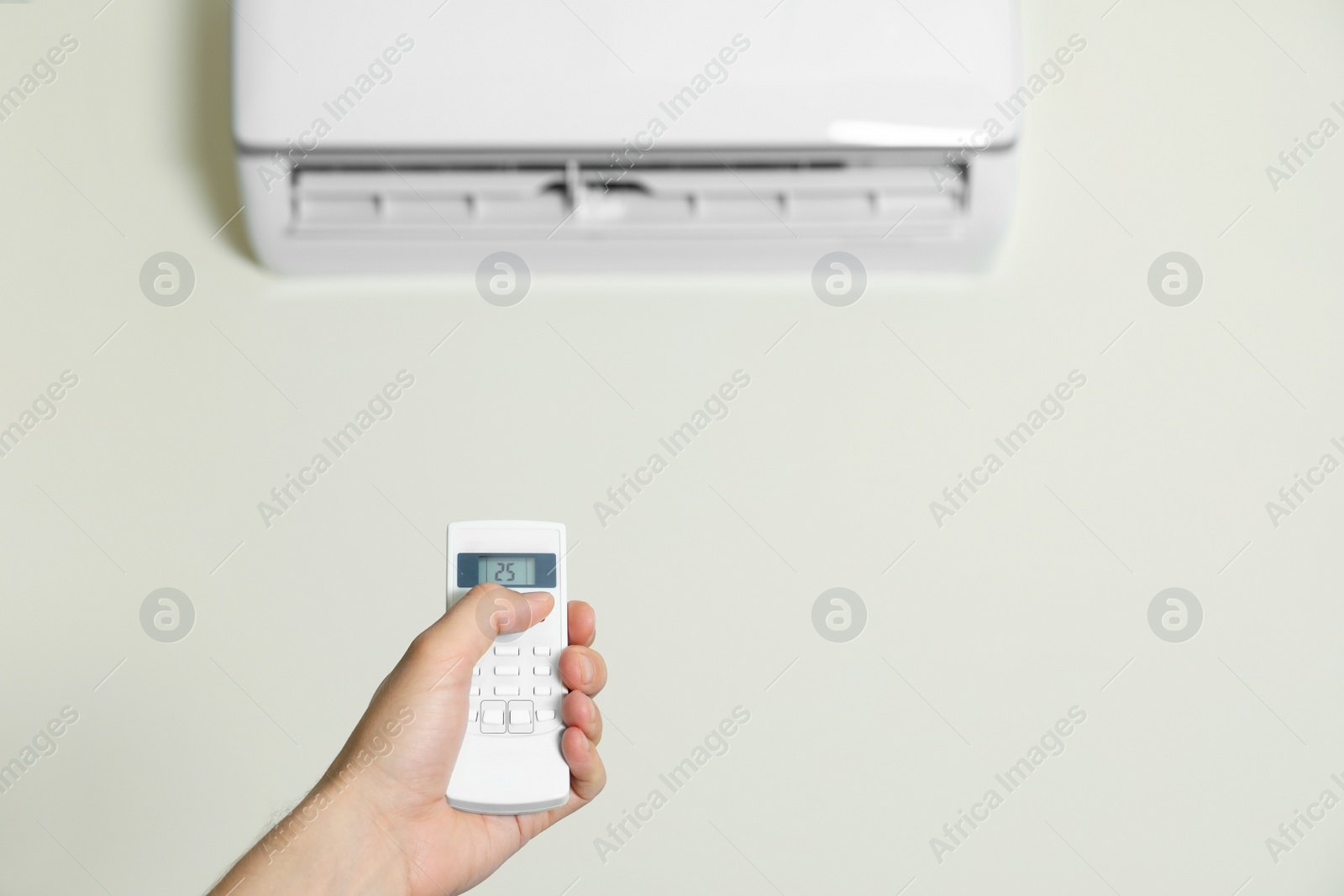 Photo of Man operating air conditioner with remote control indoors, closeup