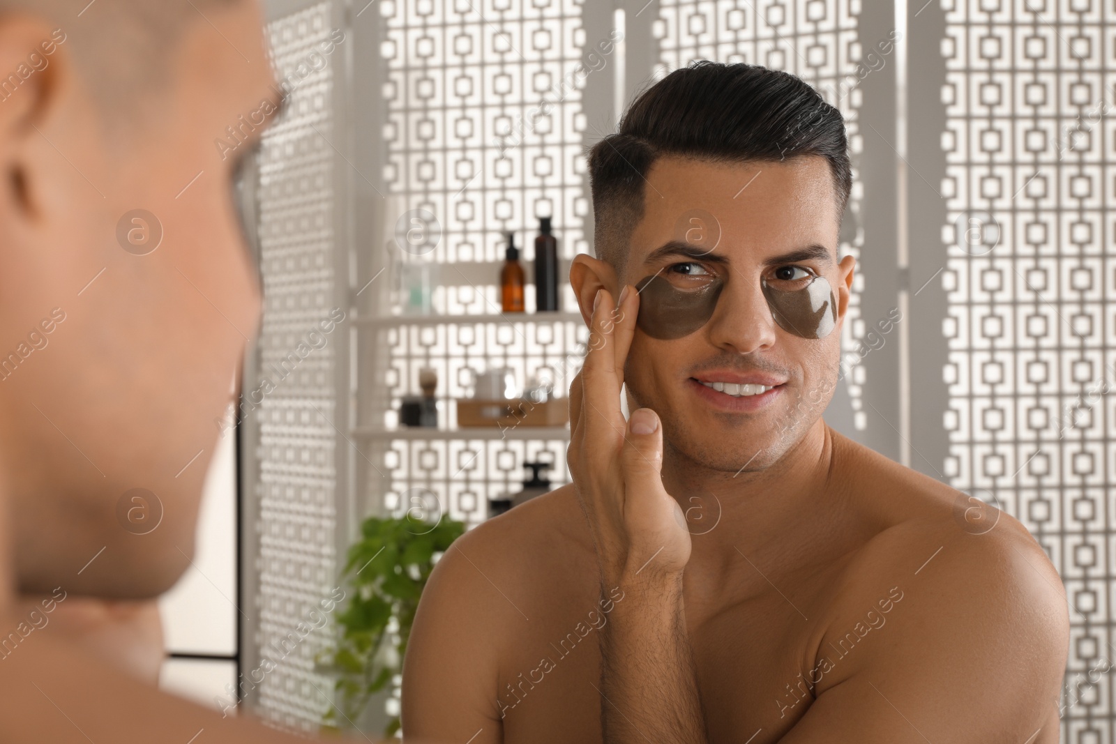 Photo of Man applying dark under eye patch near mirror at home