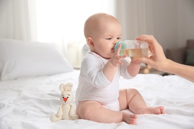 Photo of Lovely mother giving her baby drink from bottle on bed in room