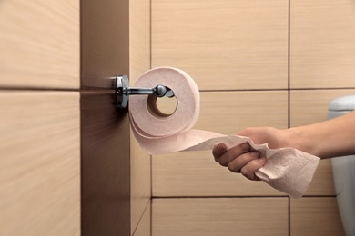 Woman pulling toilet paper from holder in bathroom