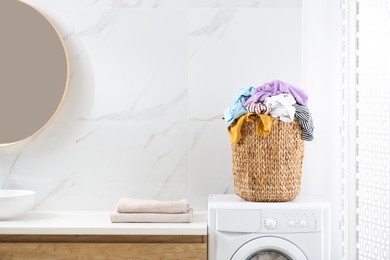 Wicker basket with dirty clothes on washing machine in bathroom. Space for text