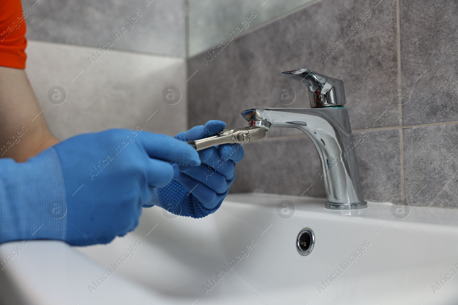 Photo of Plumber repairing faucet with spanner in bathroom, closeup