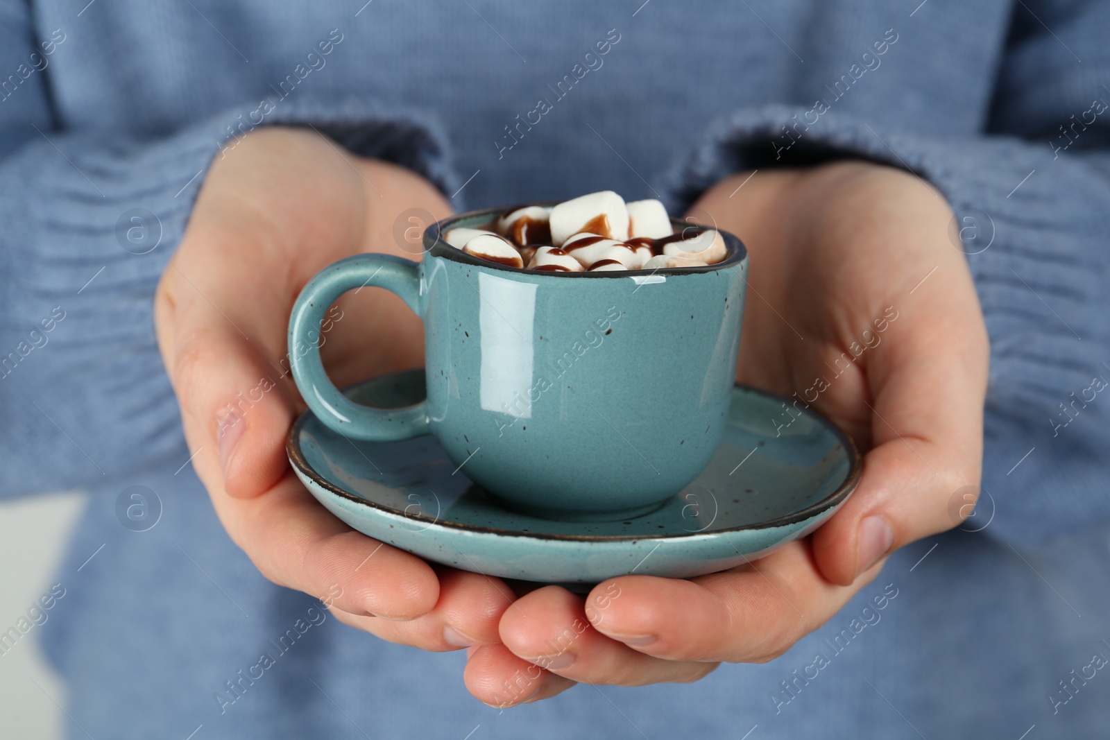 Photo of Woman holding cup of delicious hot chocolate with marshmallows and syrup, closeup