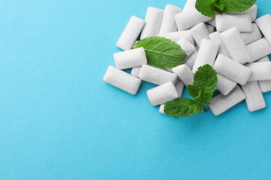Photo of Pile of tasty white chewing gums and mint leaves on light blue background, top view. Space for text