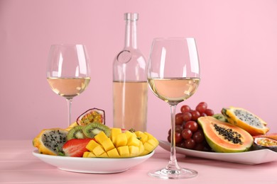 Photo of Delicious exotic fruits and glasses of wine on pink wooden table