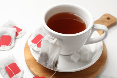 Photo of Tea bags and cup of hot beverage on white table, closeup