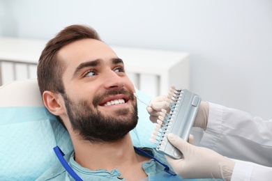 Dentist matching young man's teeth color with palette in office