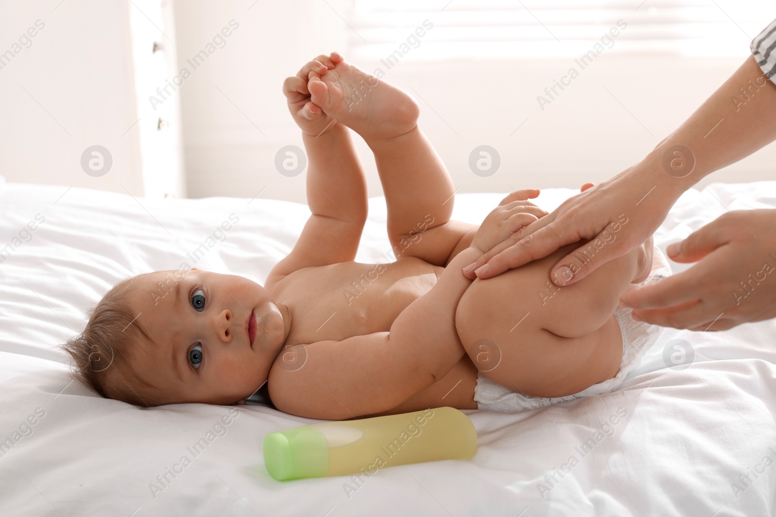 Photo of Mother massaging her cute baby with oil on bed at home, closeup