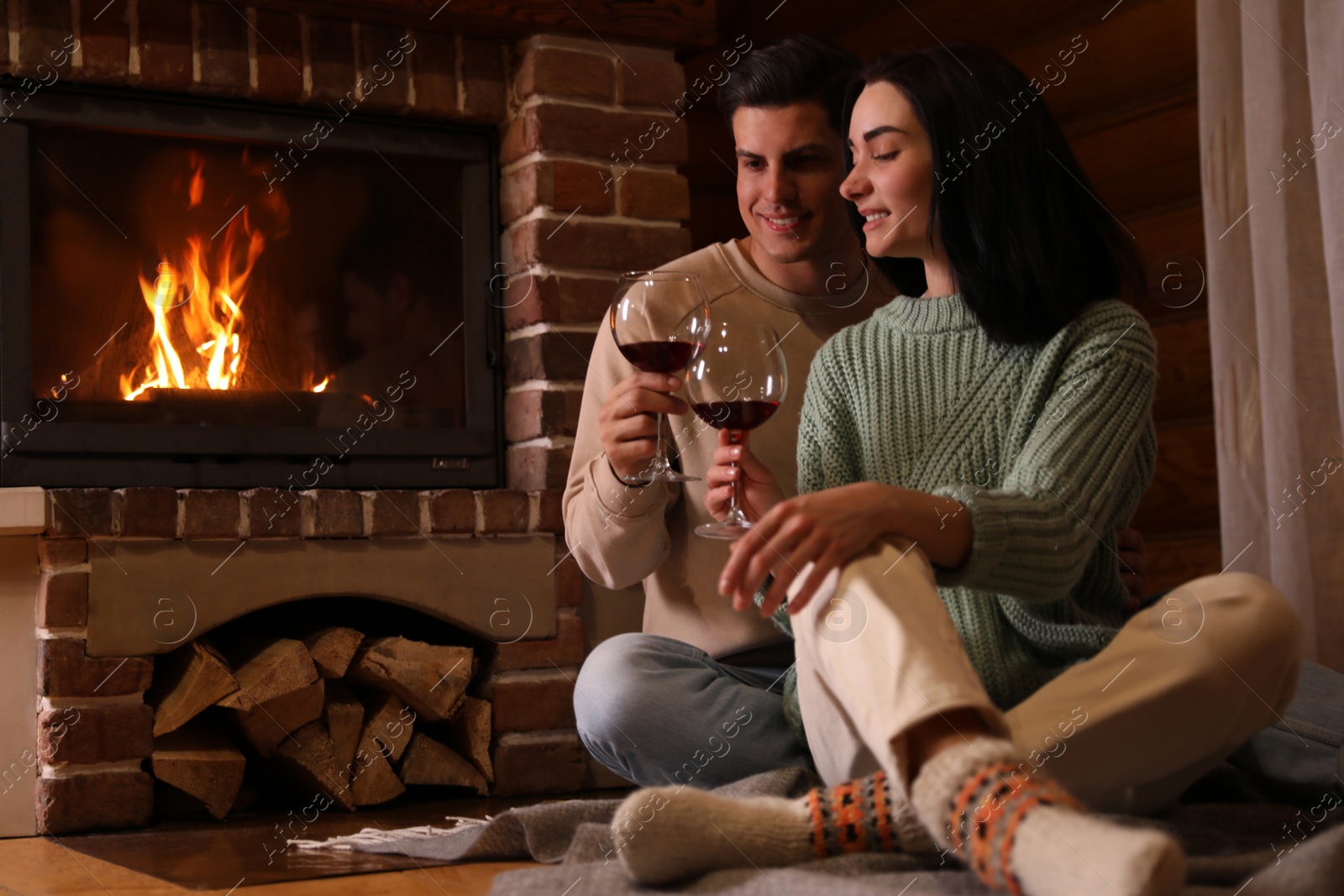 Photo of Lovely couple with glasses of wine near fireplace indoors. Winter vacation