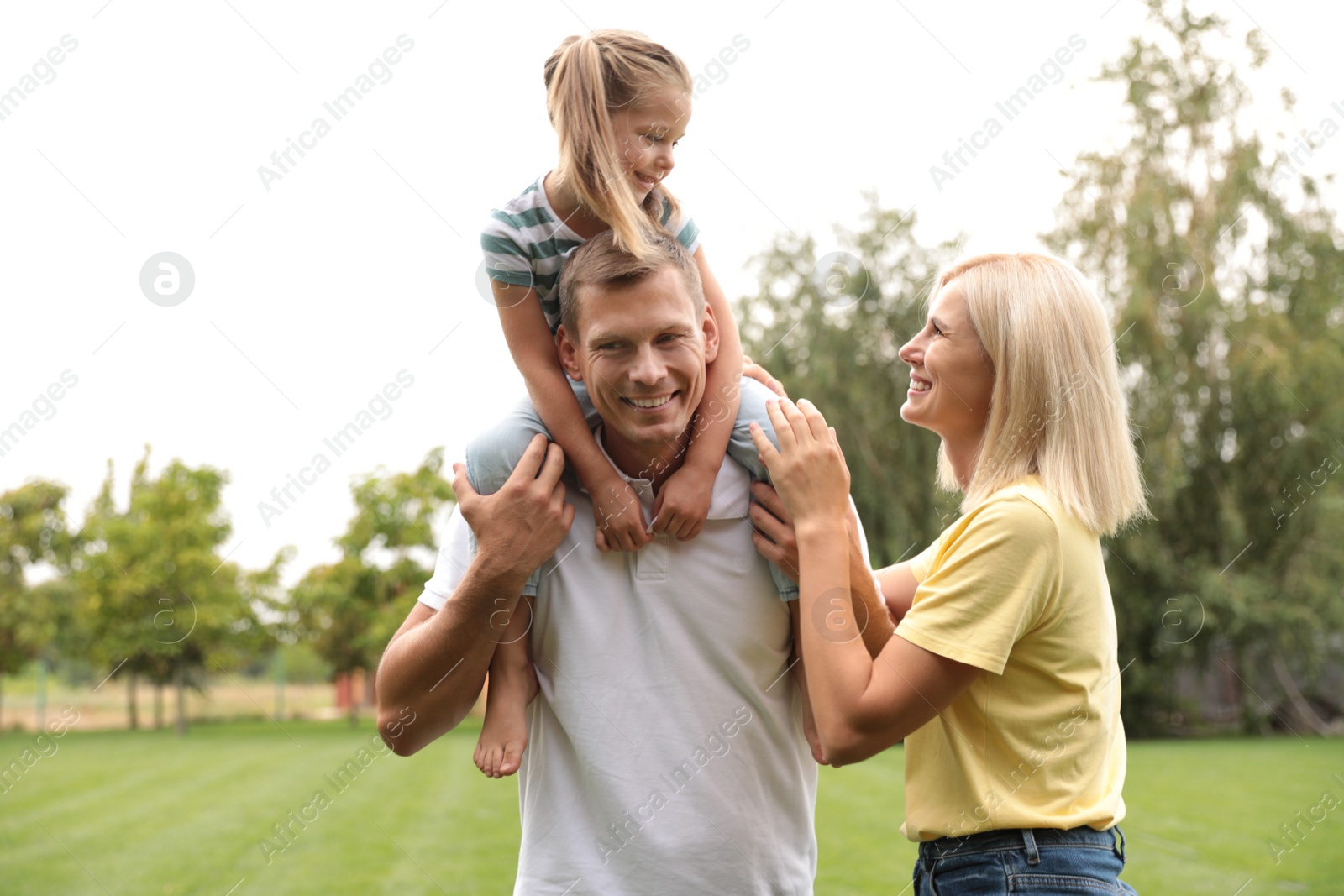 Photo of Cute little girl having fun with her parents in park on summer day