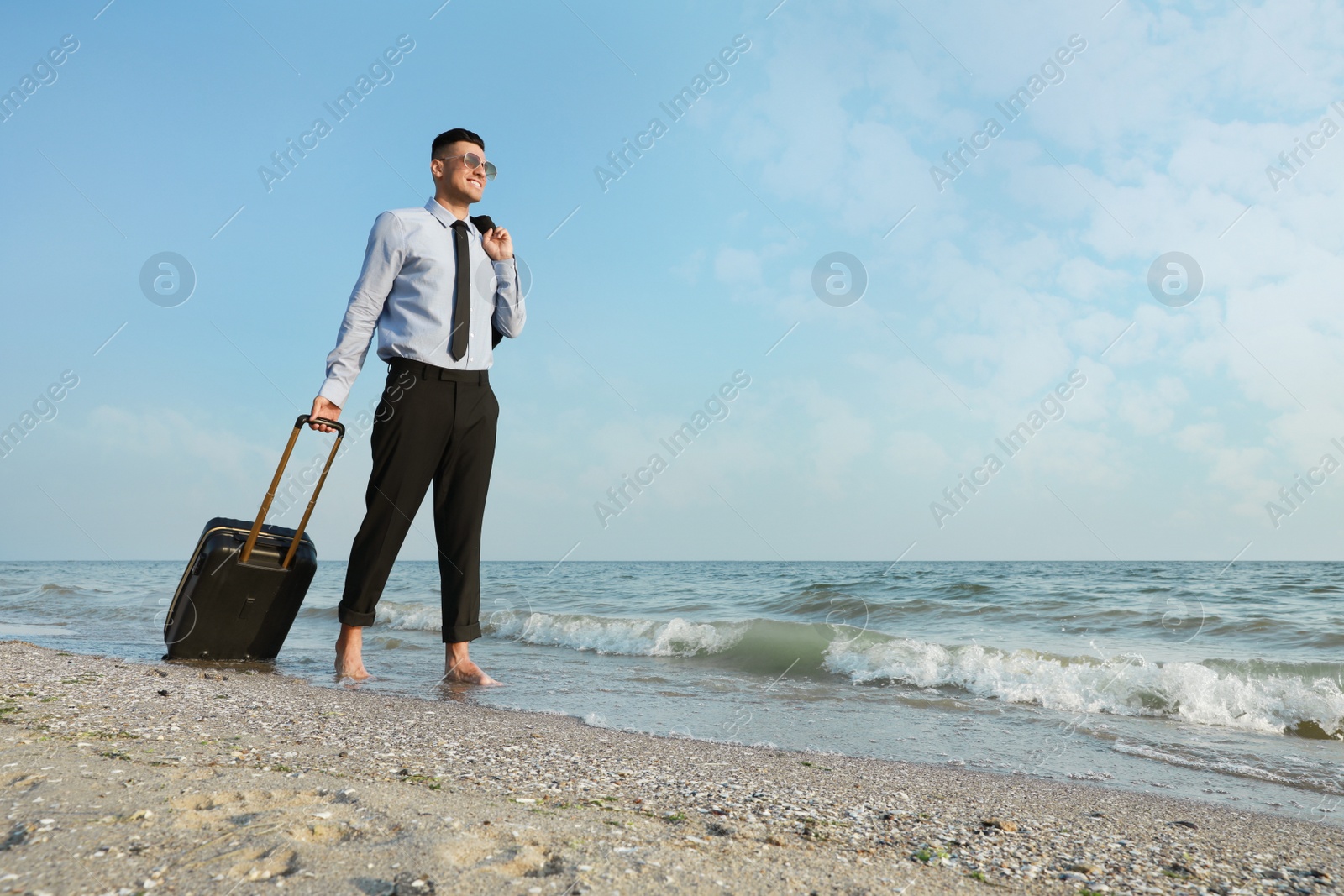 Photo of Happy businessman with suitcase walking on beach. Business trip