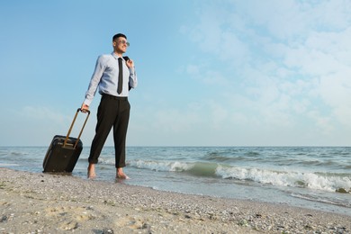 Photo of Happy businessman with suitcase walking on beach. Business trip