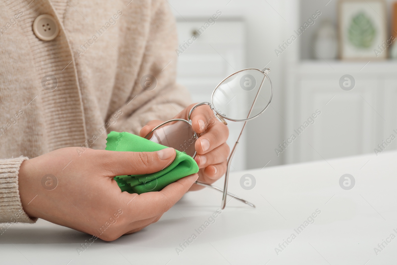 Photo of Woman wiping her glasses with microfiber cloth at white table, closeup