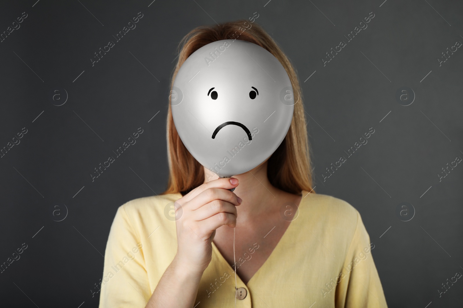 Photo of Woman hiding behind balloon with sad face on grey background. Depression concept