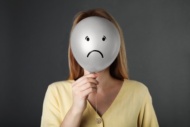 Photo of Woman hiding behind balloon with sad face on grey background. Depression concept