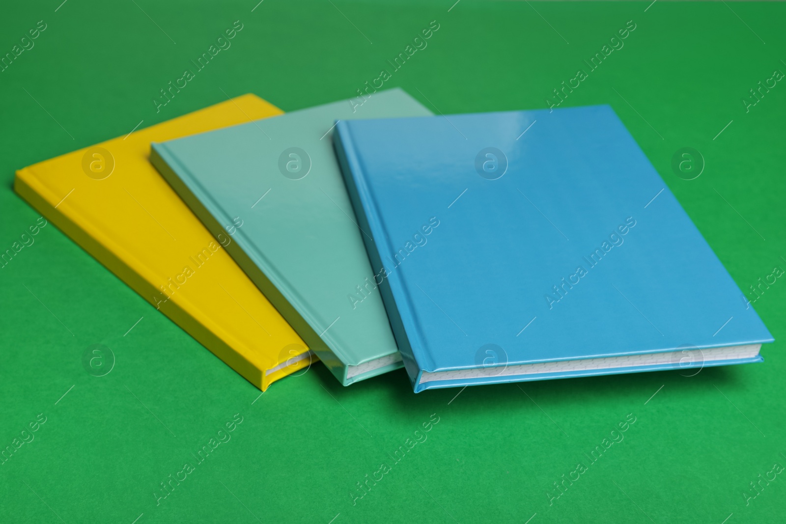 Photo of Stylish colorful planners on green background, closeup