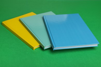 Photo of Stylish colorful planners on green background, closeup