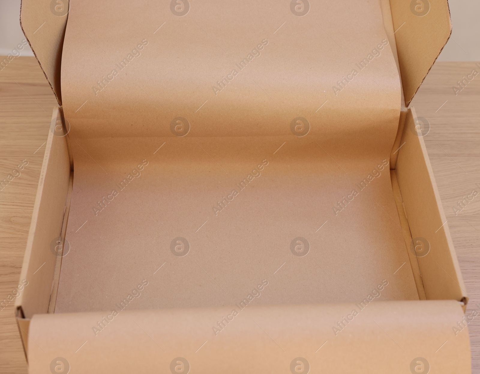 Photo of Empty cardboard box with kraft paper on wooden table. Delivery service