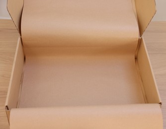 Photo of Empty cardboard box with kraft paper on wooden table. Delivery service