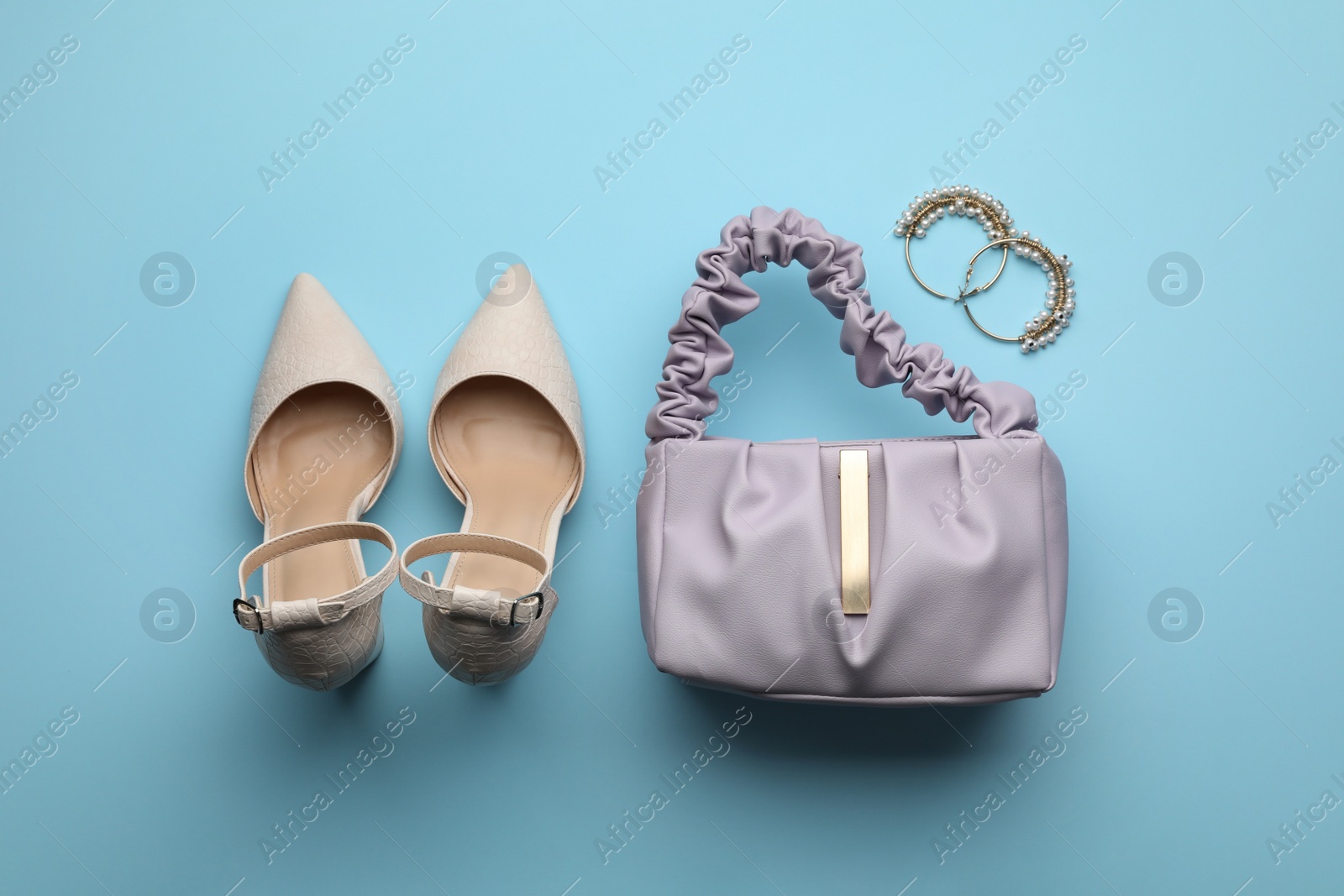 Photo of Stylish woman's bag, shoes and earrings on light blue background, flat lay