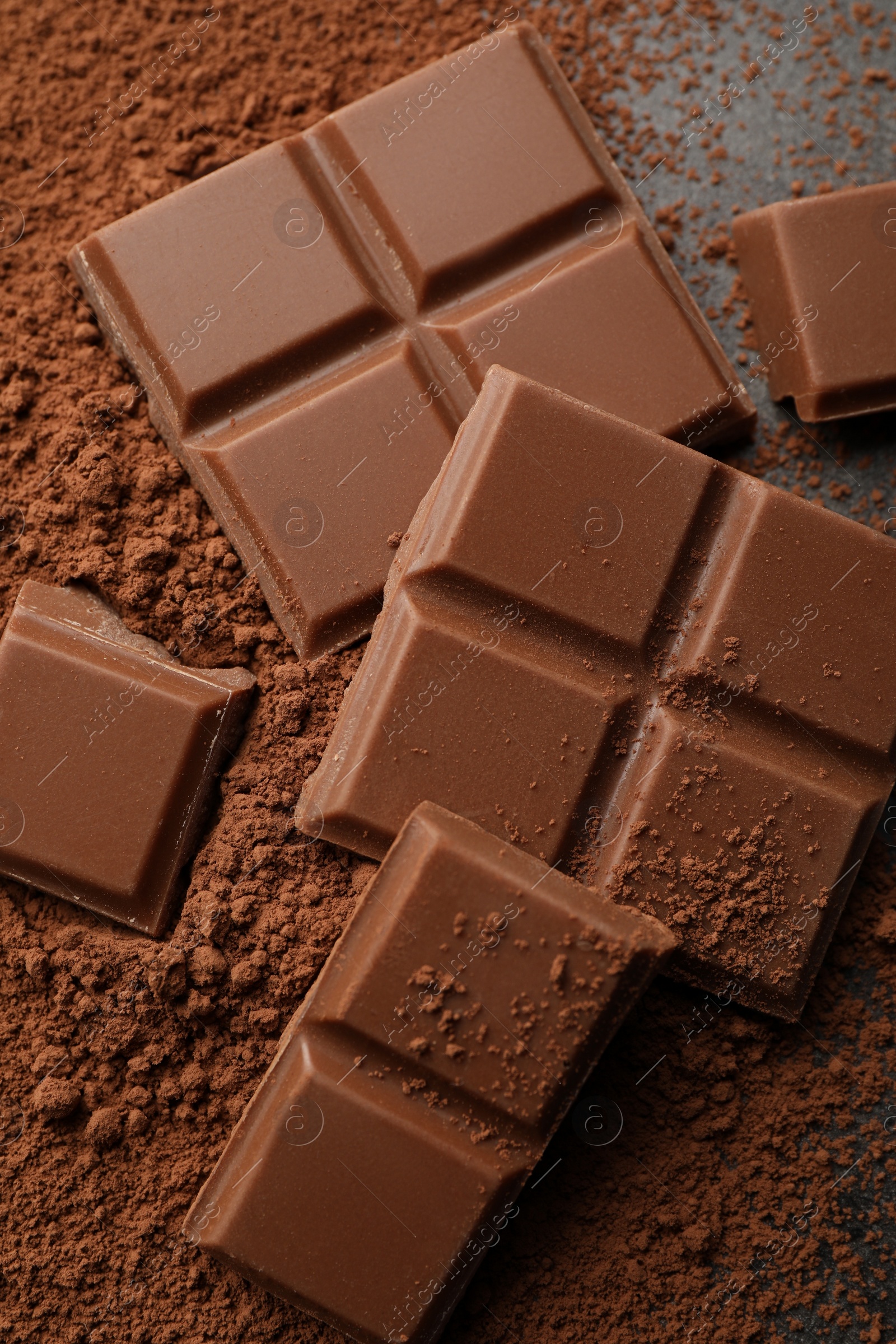 Photo of Delicious milk chocolate and cocoa powder on grey table, closeup