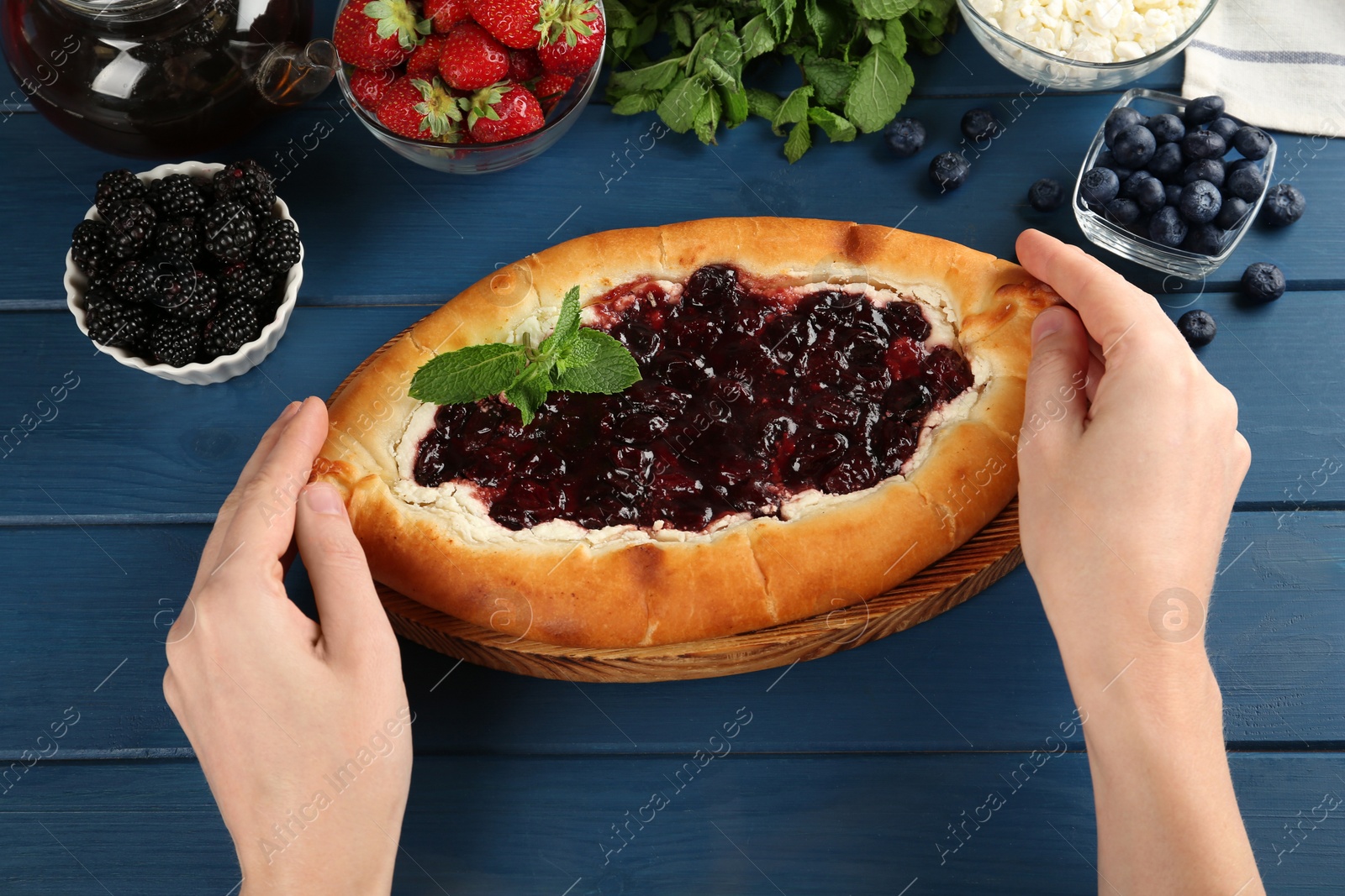 Photo of Woman eating delicious sweet cottage cheese pastry with cherry jam at blue wooden table, closeup