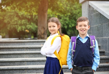 Photo of Cute school children with backpacks near stairs in park