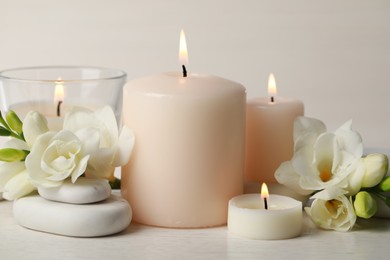 Photo of Beautiful composition with burning candles, spa stones and flowers on white table, closeup