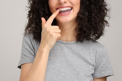 Photo of Young woman applying whitening strip on her teeth against light grey background, closeup