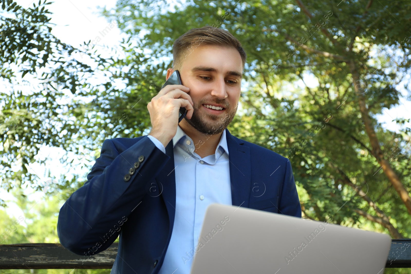 Photo of Young man talking on smartphone while working with laptop in park