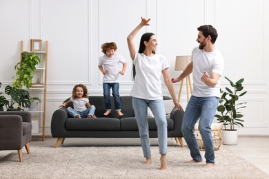 Happy family having fun in living room. Couple dancing while children jumping on sofa