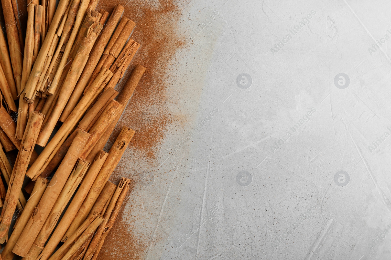 Photo of Aromatic cinnamon sticks and powder on grey table, flat lay. Space for text