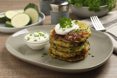 Delicious zucchini fritters with sour cream served on wooden table