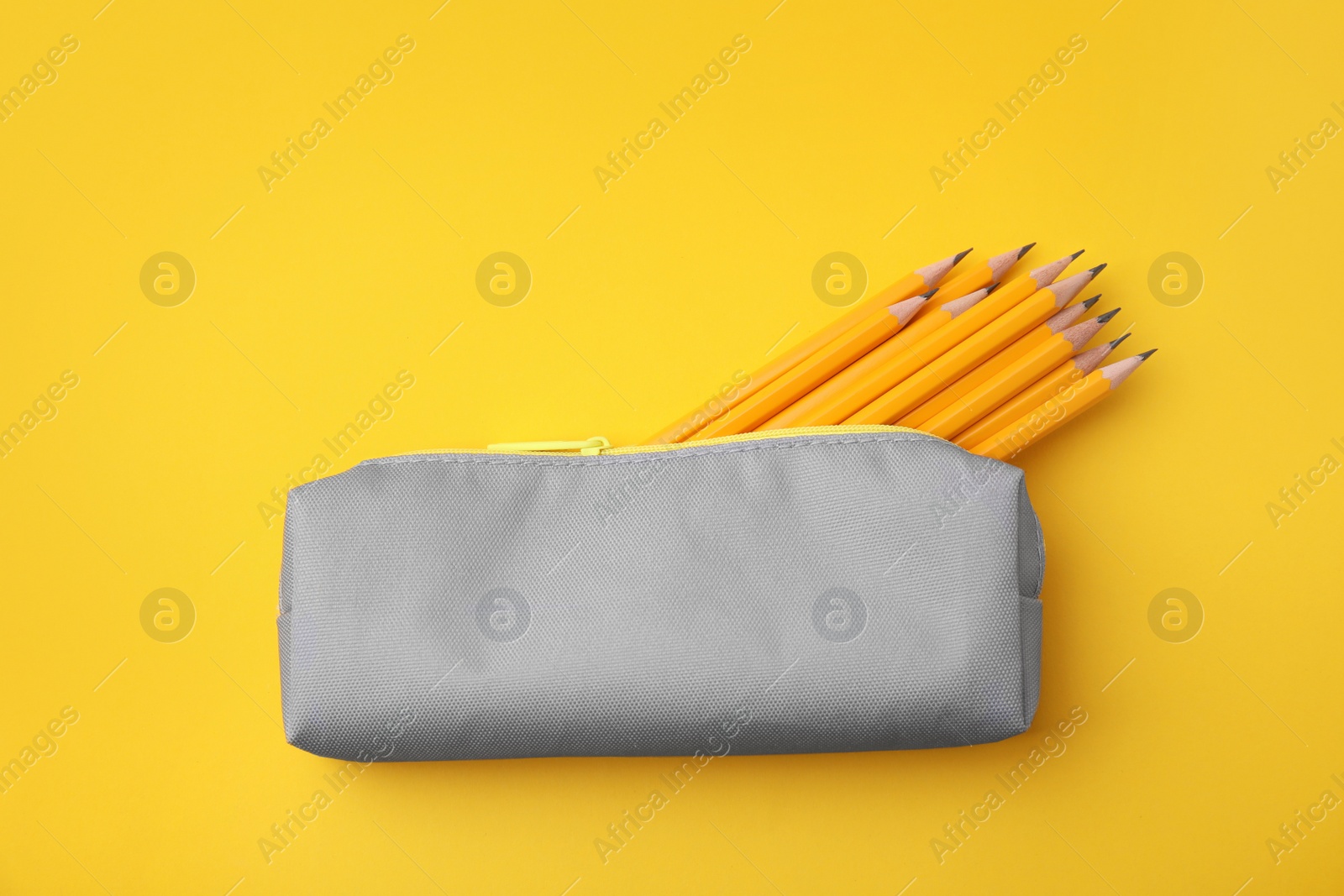 Photo of Many sharp pencils in pencil case on yellow background, top view