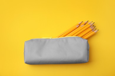 Many sharp pencils in pencil case on yellow background, top view