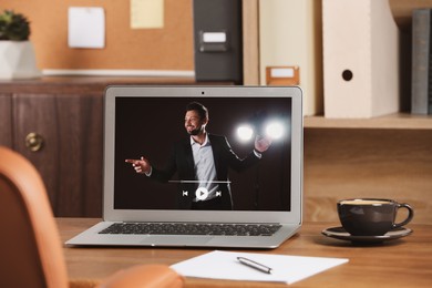 Image of Laptop with performance of motivational speaker on wooden table indoors
