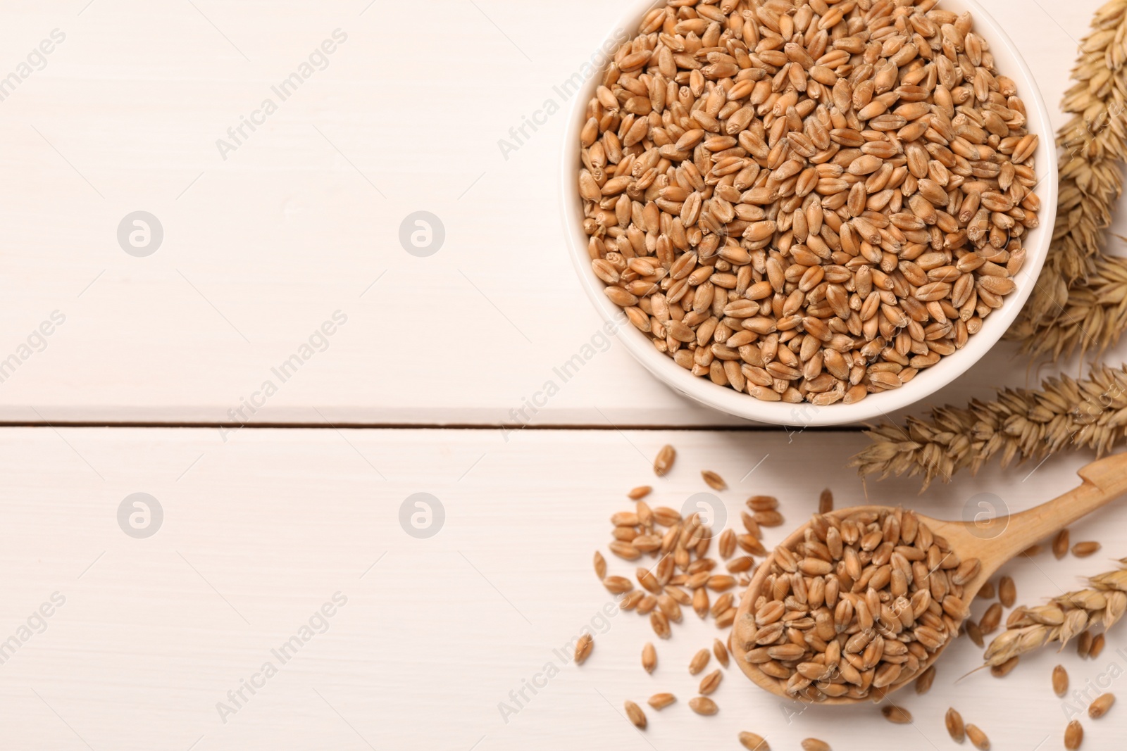 Photo of Wheat grains on white wooden table, flat lay. Space for text