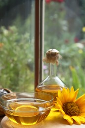 Photo of Organic sunflower oil and flower on wooden table, space for text