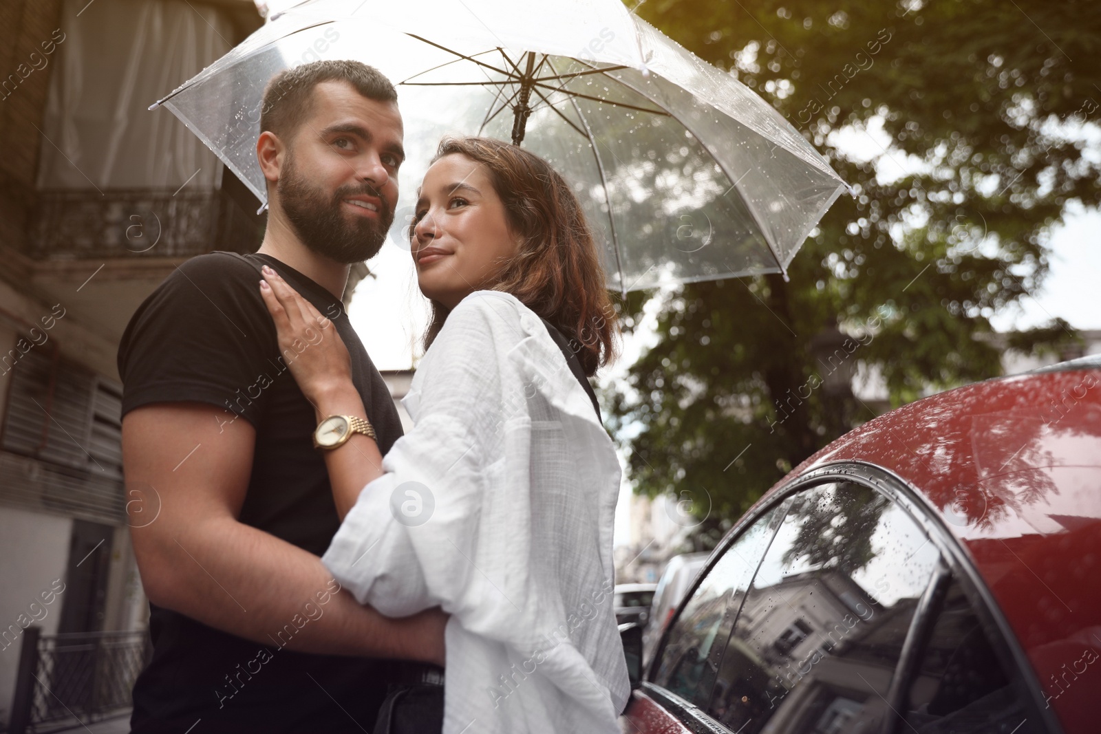 Photo of Young couple with umbrella enjoying time together under rain on city street, space for text