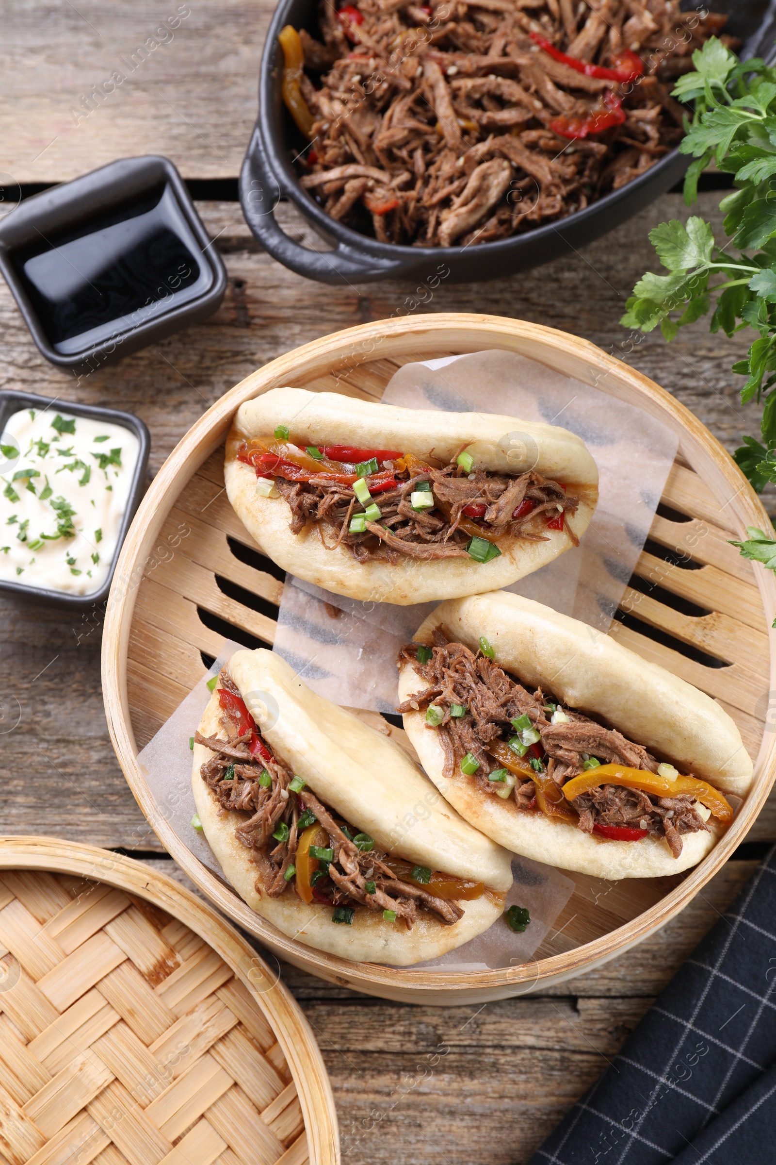 Photo of Delicious gua bao in bamboo steamer on wooden table, flat lay