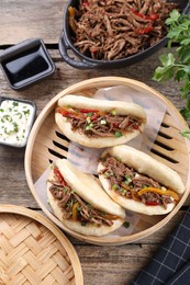 Delicious gua bao in bamboo steamer on wooden table, flat lay