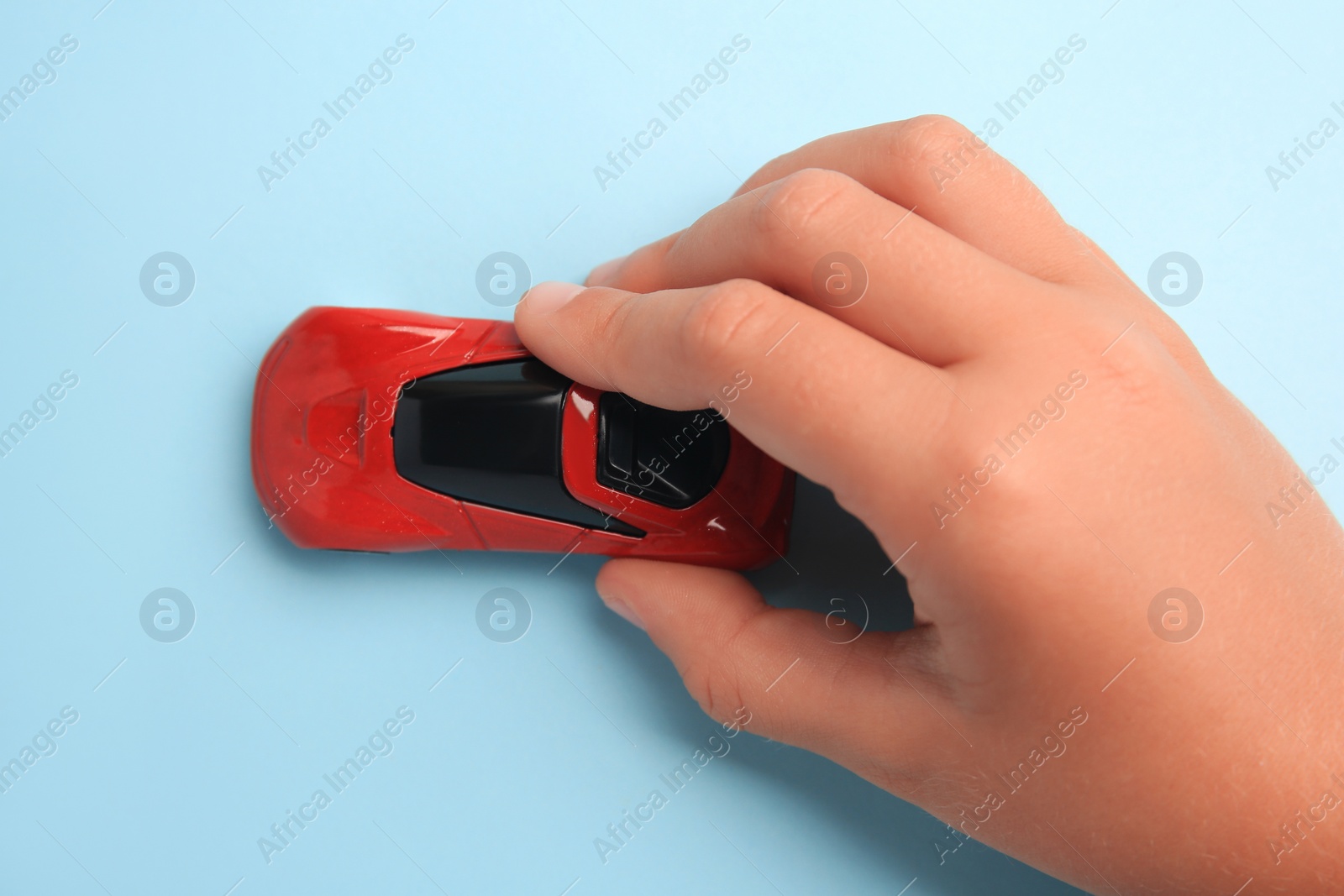 Photo of Child playing with toy car on light blue background, top view