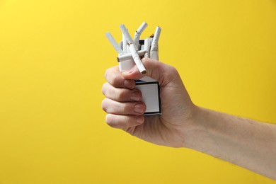 Photo of Stop smoking. Man holding pack with broken cigarettes on yellow background, closeup